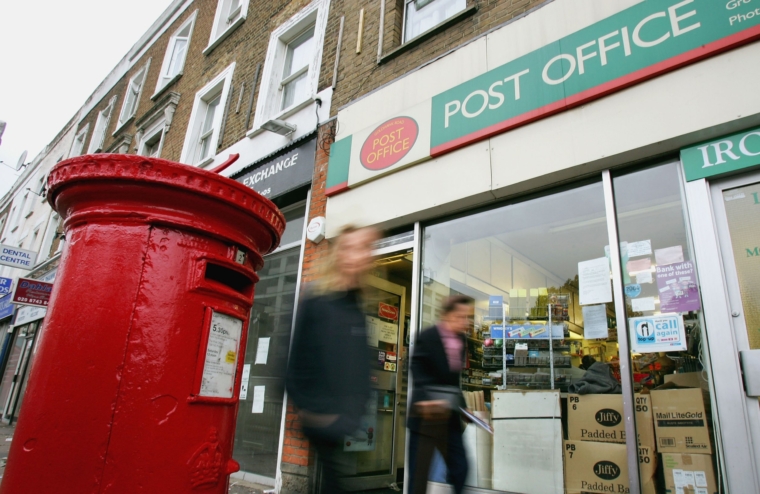 Londyn - 1 listopada 2004 r.: Ludzie przechodzą obok urzędu pocztowego na Main Street 1 listopada 2004 r. w Londynie w Anglii.  Royal Mail odrzuciła doniesienia, że ​​jest bardzo blisko lub sprzedaje od 240 do 270 swoich dużych oddziałów, tracąc 70 milionów funtów rocznie.  (Zdjęcie: Scott Barbour/Getty Images)